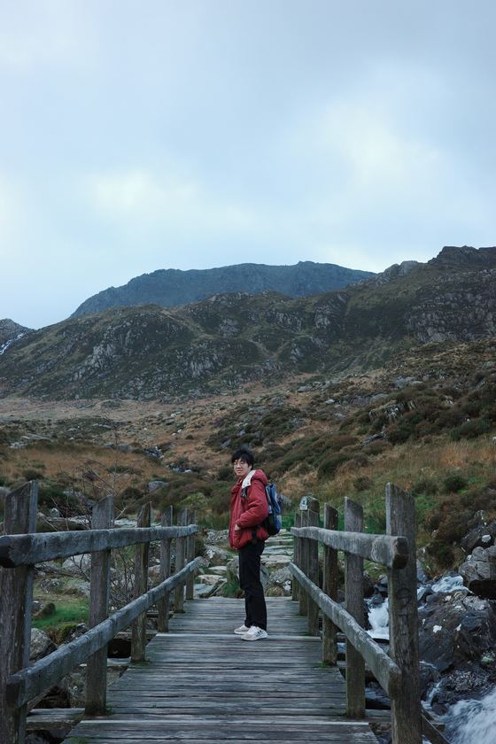 Snowdonia and Llanfairpwll: Hiker on bridge beneath mountain ridge